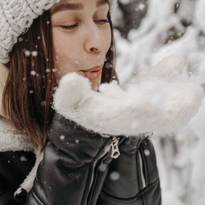Eine verliebte Frau bläst ihre Handschuhe voller Schnee